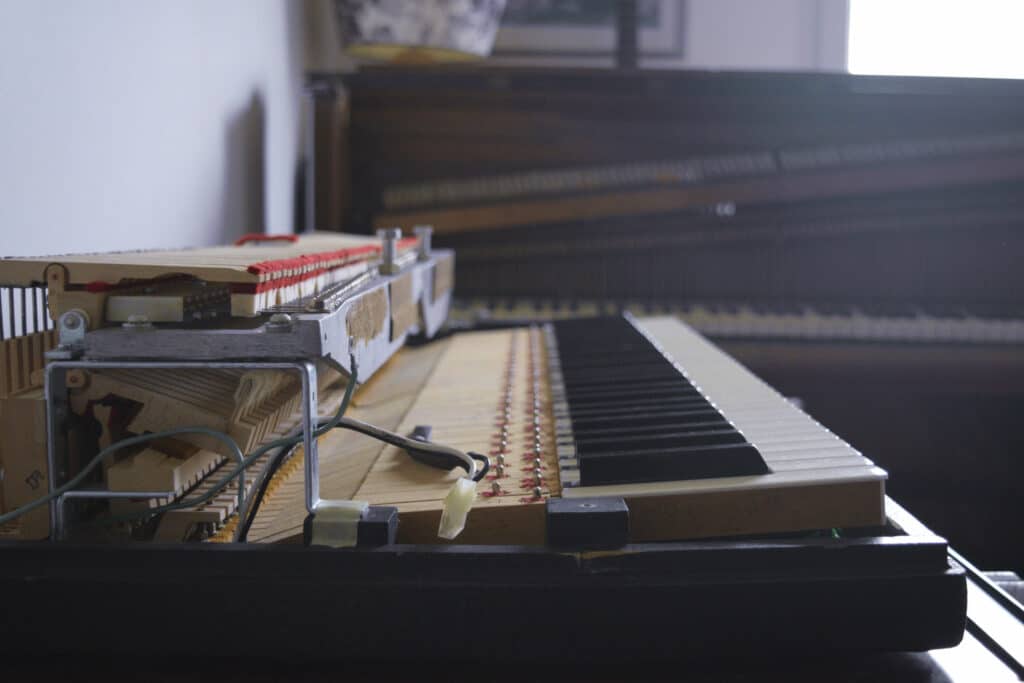 Photo du clavier et de la mécanique d'un Wurlitzer 200A en cours d'entretien, à l'arrière-plan, on peut voir un pianino Roller & Blanchet ouvert.